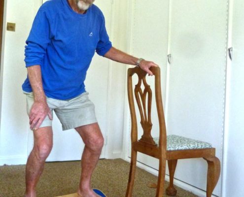 Peter Smith, 75, on his CoolBoard Wobble Board. He is doing balance exercise for elderly on the Easy Start Balance Disc using a chair for support.