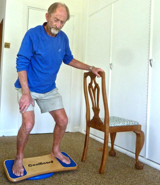 Peter Smith, 75, on his CoolBoard Wobble Board. He is doing balance exercise for elderly on the Easy Start Balance Disc using a chair for support.