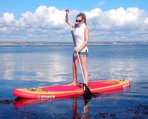 Lady on her Stand Up Paddle Board using her balance training to balance on her SUP on the sea