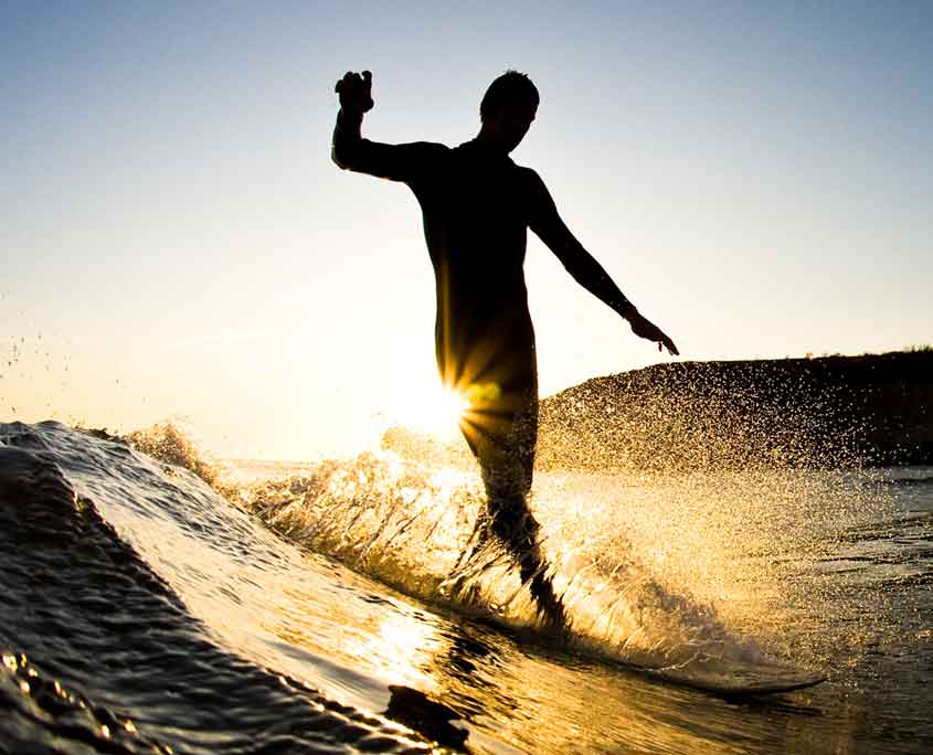 image of surfer at sunset cross stepping on surf board